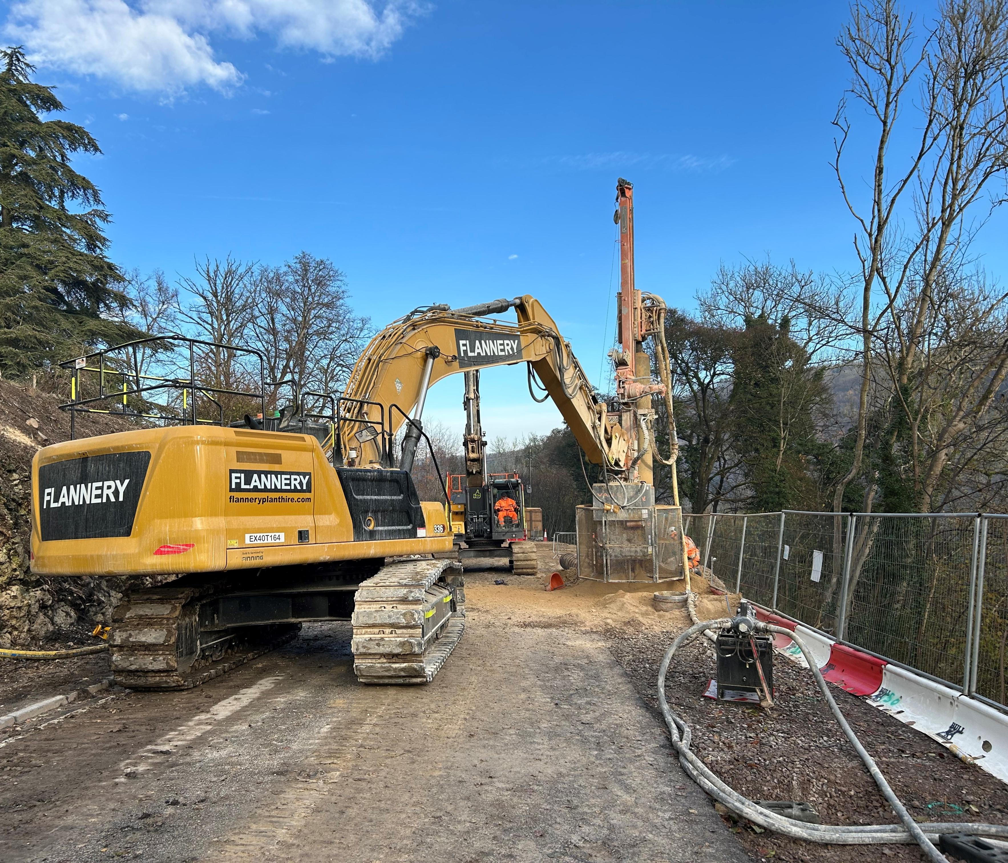 Photo shows a 35t excavator, drilling the rock sockets as part of the piling installation to support the A36 road embankment