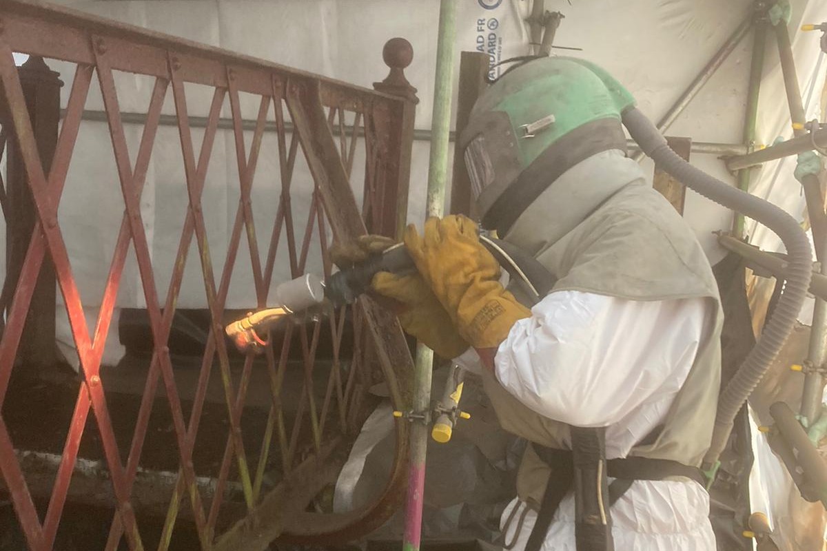 Colleagues wearing protective clothing to remove lead paint and corrosion