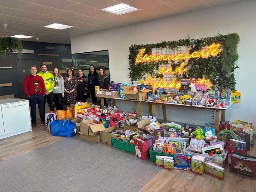 Staff stand next to a collection of toys and food for families in need at Christmas.