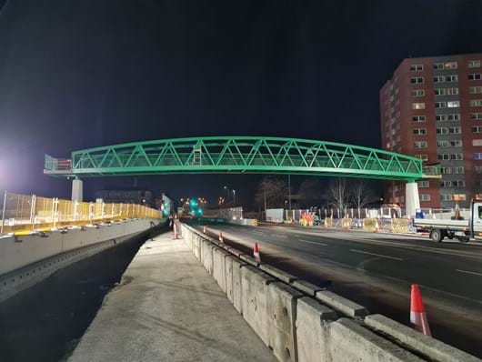Construction of new footbridge, green steel, roadworks, night time.