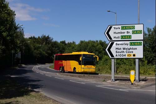 Yellow school bus on A63, blue sky with trees in the background, road signage pointing left.