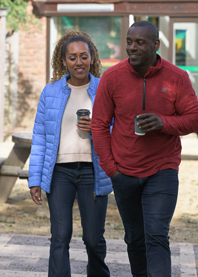 Man and woman walking each holding a drink