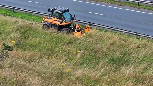 An orange piece of machinery, or a robot cutter, taking a cut of wildflowers alongside the A56 in Kancashire