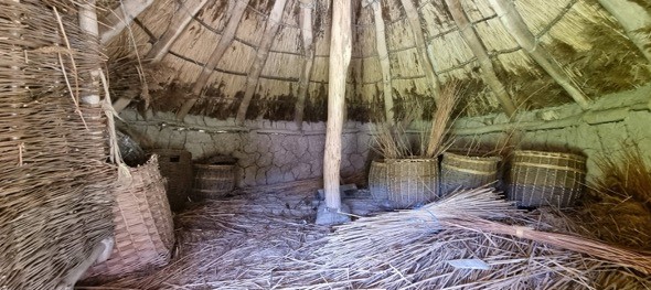 Reconstruction of a Roundhouse, with lots of straw on the floor and a long piece of wood supporting the structure from the middle
