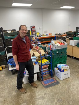 Food bank volunteer stands next to stack of donated food.